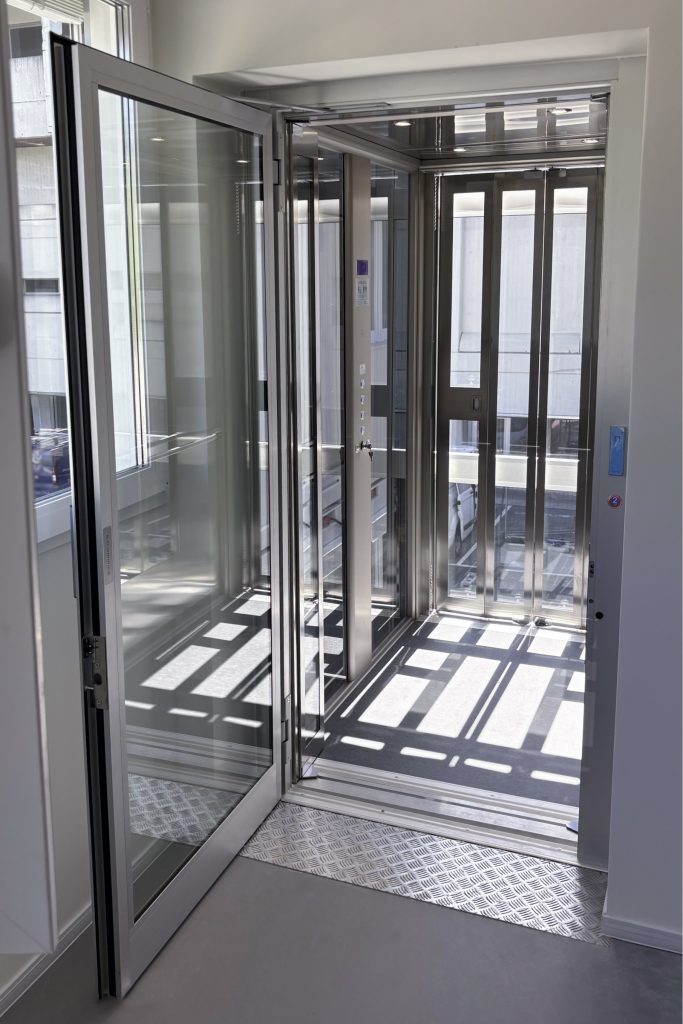 Home lift Eltec Lift HLB elettrico con struttura TA, vetro fumé e porte a soffietto inox in cabina; soluzione su misura che unisce accessibilità, comfort e design integrato. Vista interna dell'impianto.